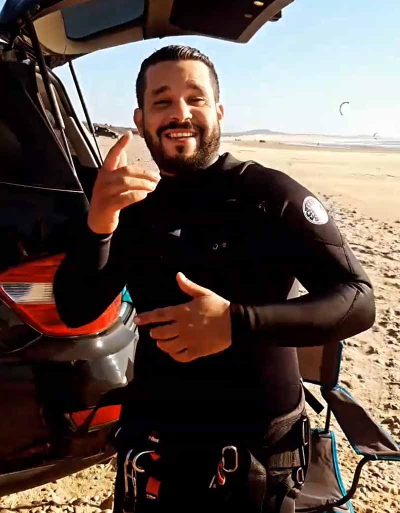 Homme en combinaison et harnais de kitesurf heureux sur la plage.